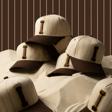 Load image into Gallery viewer, Three baseball caps with brown brims on a white surface against a striped brown background
