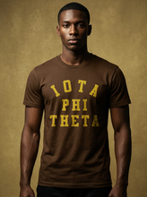 Load image into Gallery viewer, Man wearing a brown t-shirt with 'IOTA PHI Theta' text against a beige background
